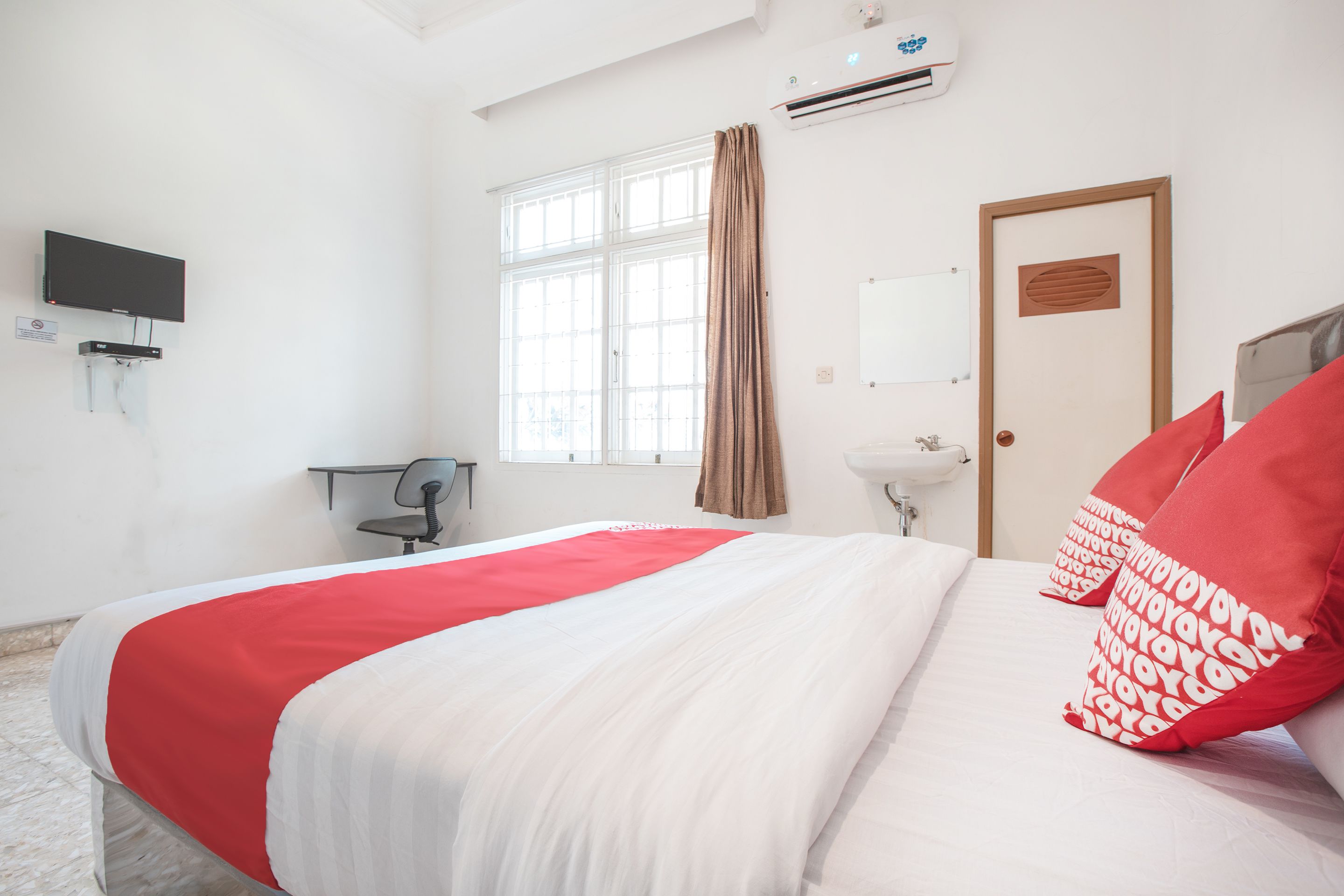 Een hotelkamer met een groot bed, een televisie, een bureau en een raam met gordijnen.