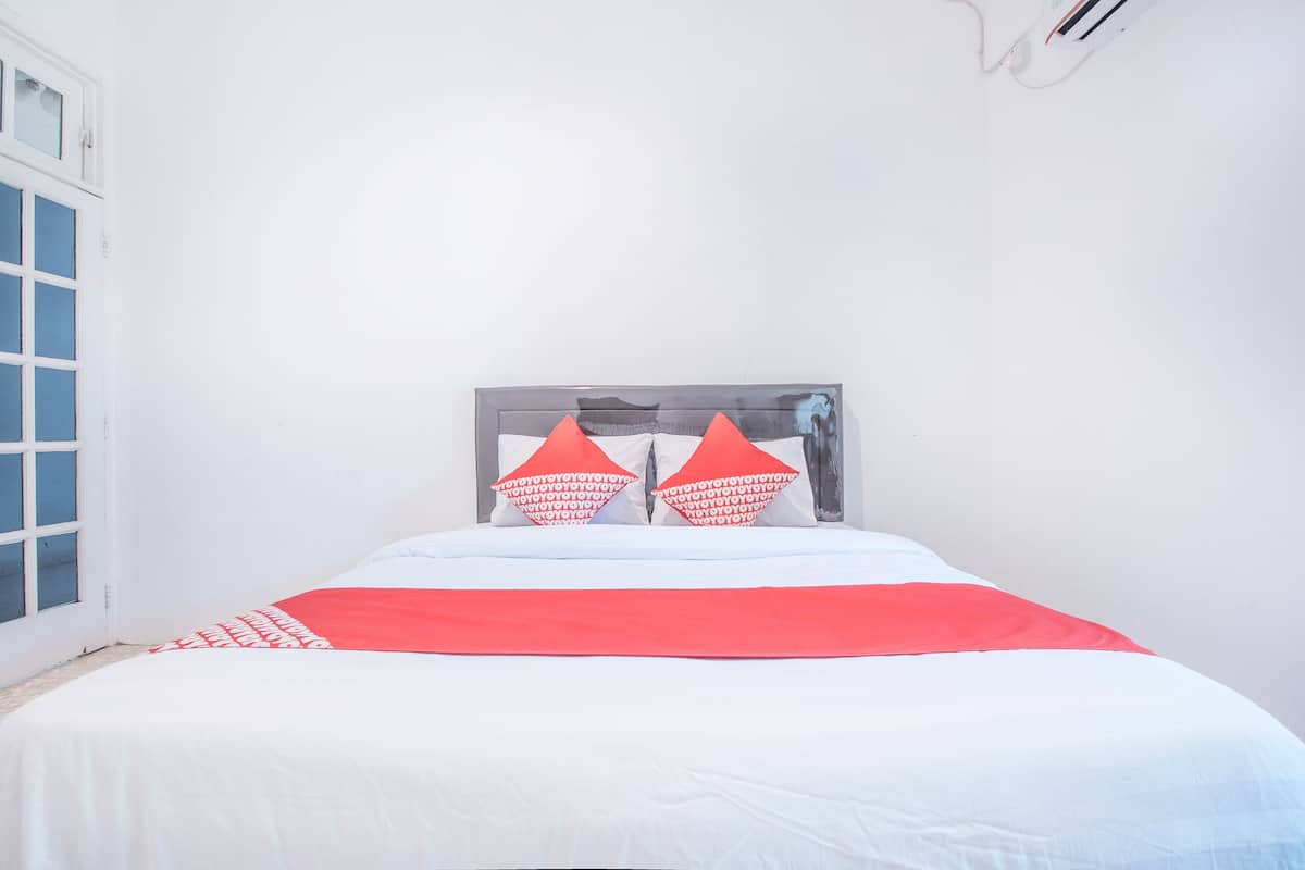 Un lit avec une couvre-lit blanche et rouge, deux oreillers rouges et une tête de lit grise.