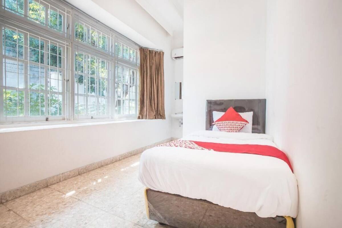 Une chambre d’hôtel avec une grande fenêtre, un lit recouvert d’une couette rouge et blanche, et une tête de lit agrémentée d’un coussin rouge.