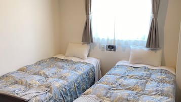 A hotel room with two beds, a small table, and a window with curtains.