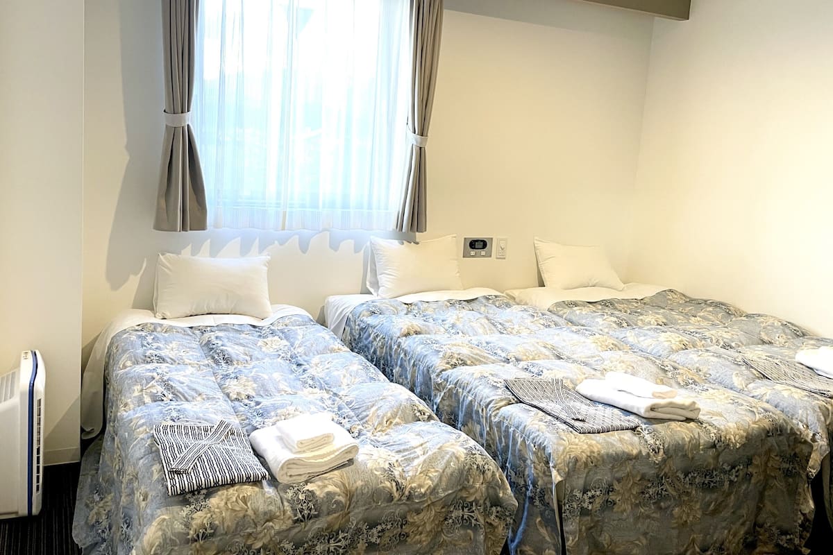Een hotelkamer met twee bedden, een raam met gordijnen, een thermostaat en een radiator.