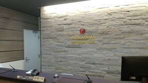 Een receptiebalie bij Hotel Murayama Nishiguchi, met een stenen muur op de achtergrond, een naamplaatje, een telefoon en een computerscherm.