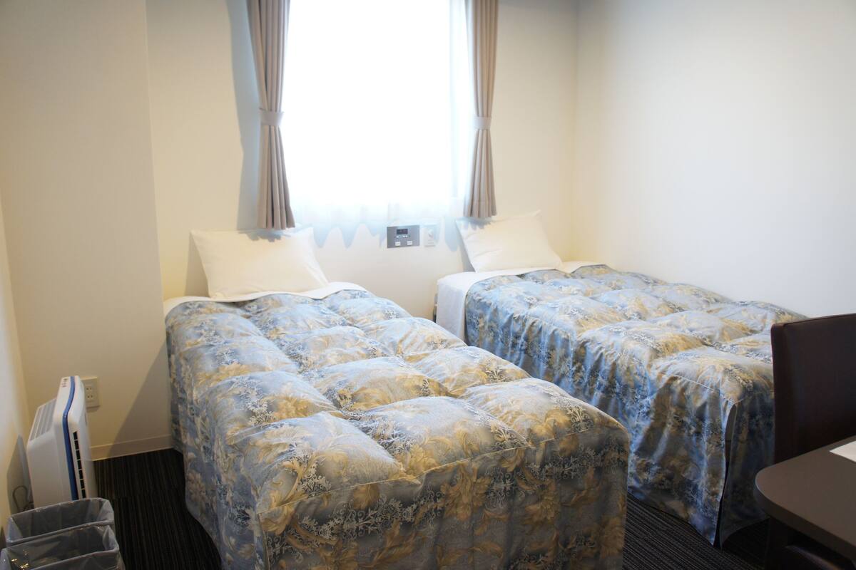 Een hotelkamer met twee bedden, een bureau en een raam met gordijnen.