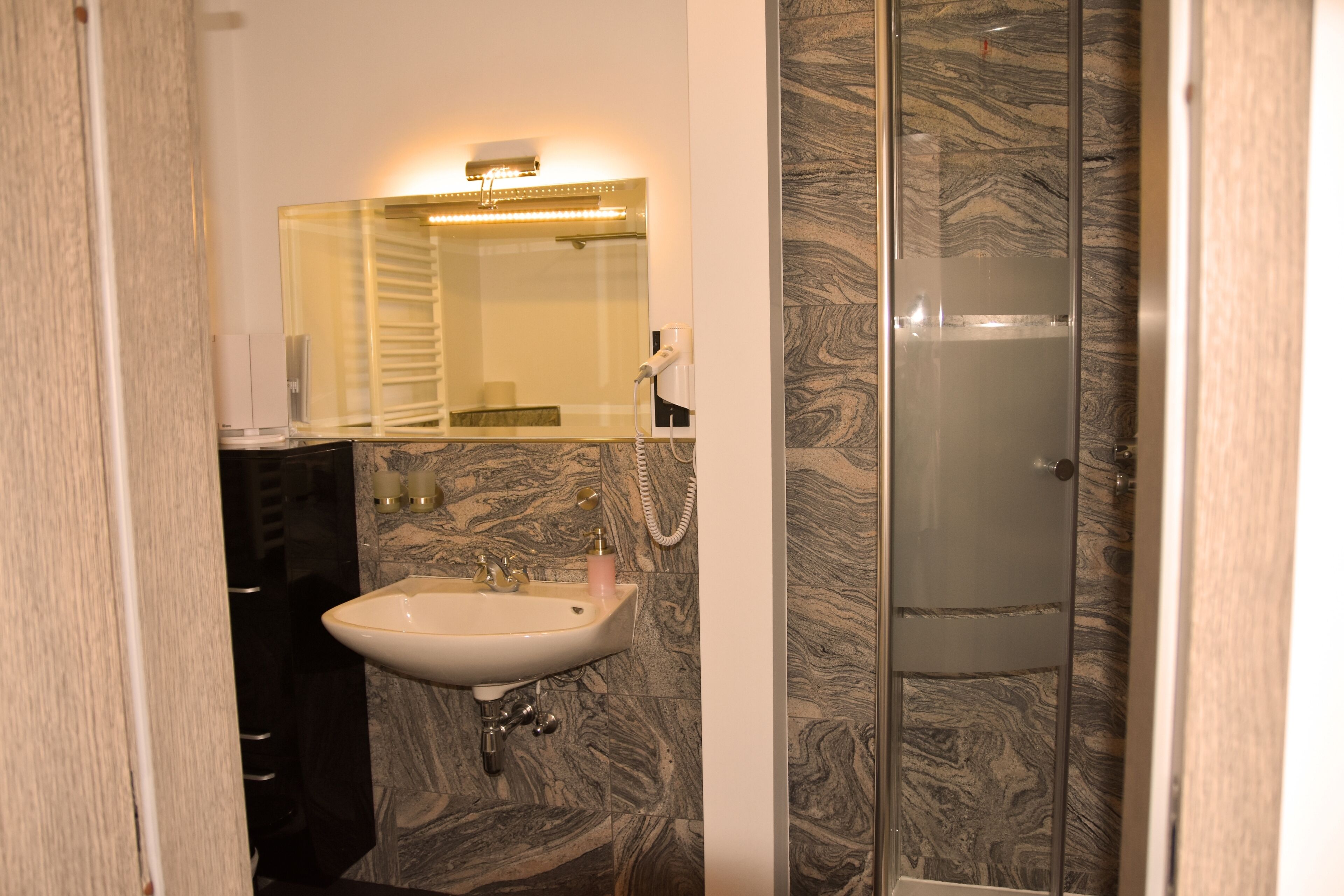 A bathroom with a marble sink, a mirror, and a glass shower enclosure.