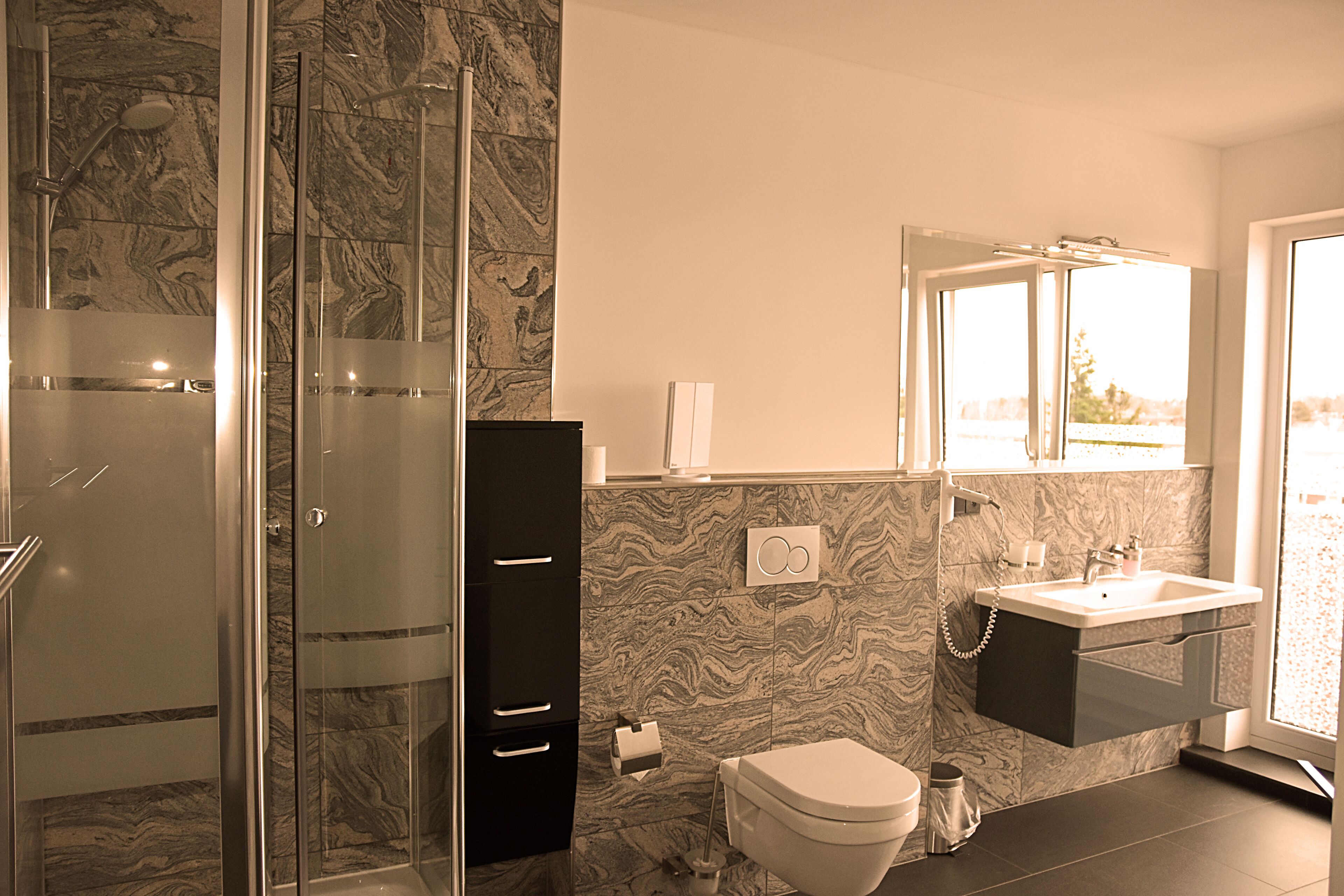 Un baño con cabina de ducha de vidrio, pared con diseño de mármol, inodoro y lavabo con espejo superior.