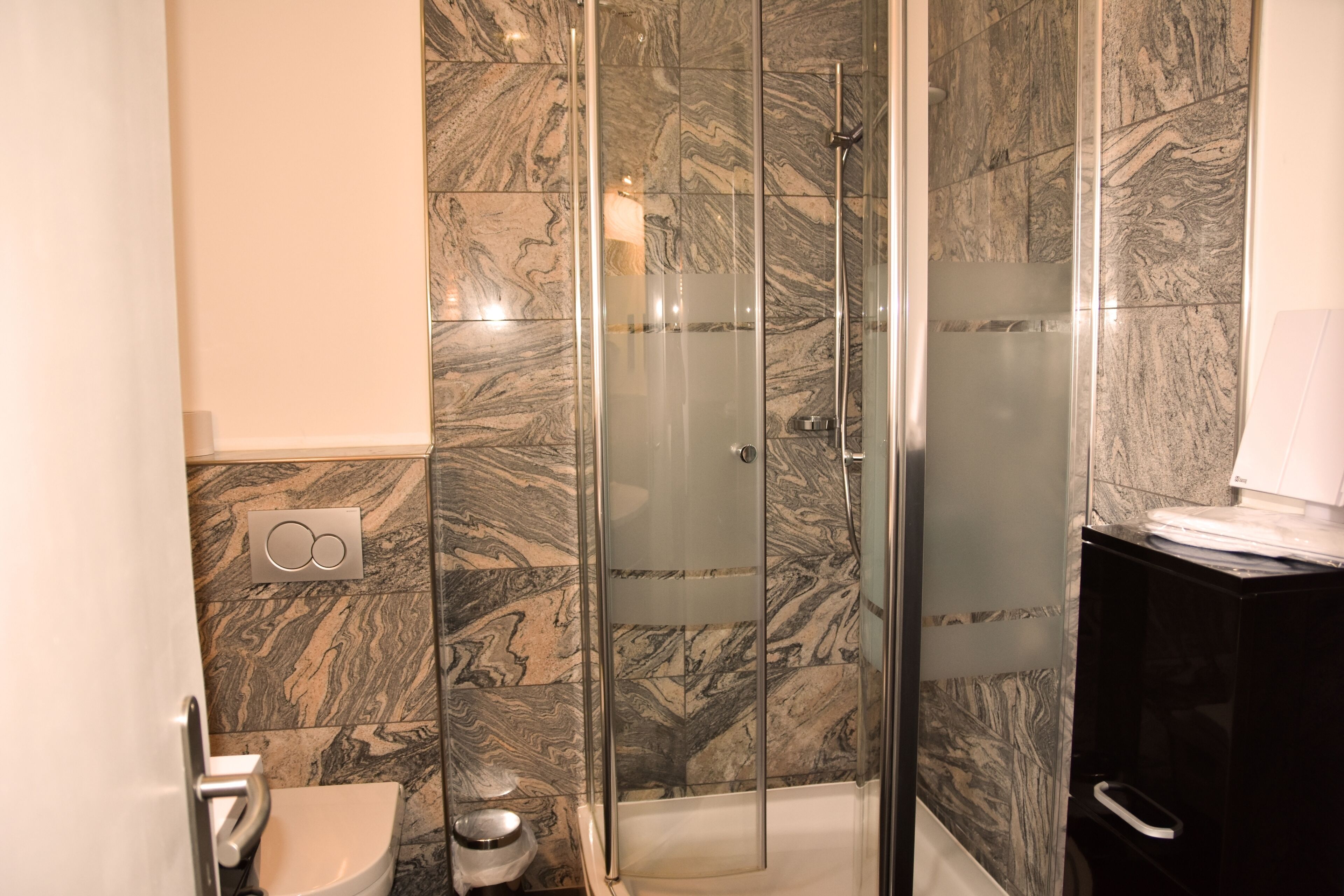 Ein Badezimmer mit Duschkabine, Marmorfliesen, Toilette und Waschbecken.