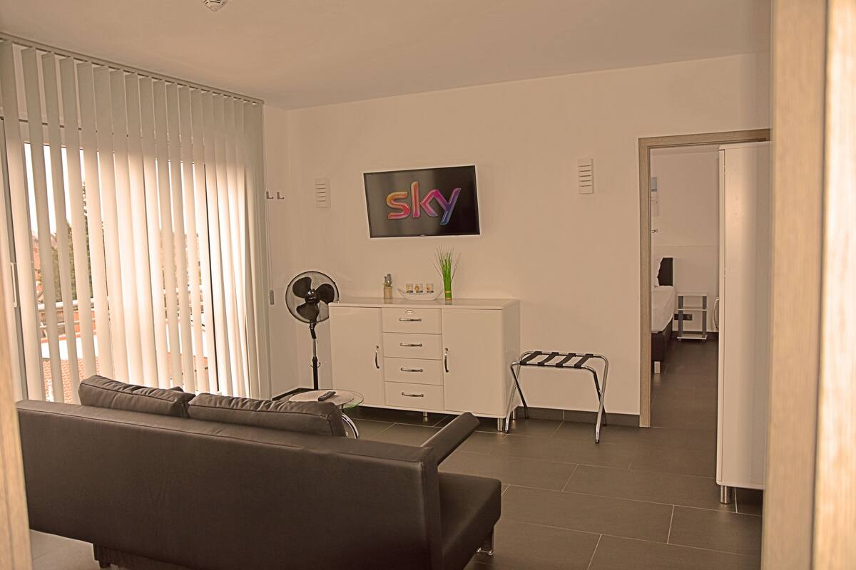 Una sala de estar moderna con un sofá, un televisor montado en la pared, un ventilador y una mesita con adornos.