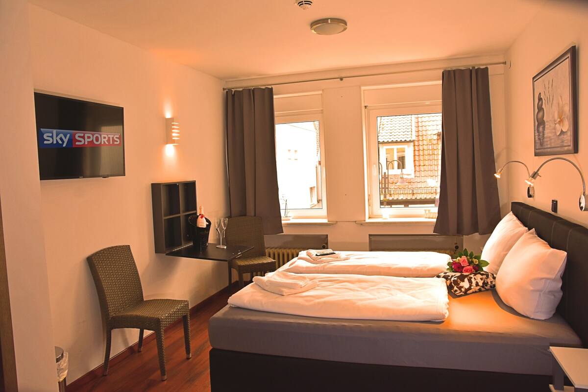 Habitación de hotel con cama, una silla, televisor y ventana con cortinas.