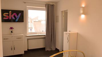 A bedroom with a bed, a dresser, a radiator, a window with curtains, a wall-mounted TV, and a mirror.