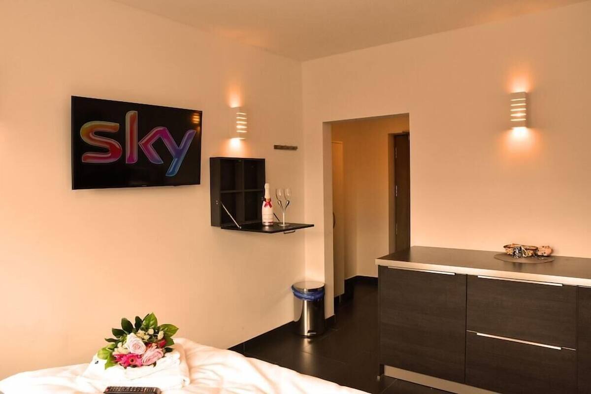Una habitación de hotel moderna con una cama, una mesita de noche, un aparador, un televisor montado en la pared y un letrero que dice 'sky'.