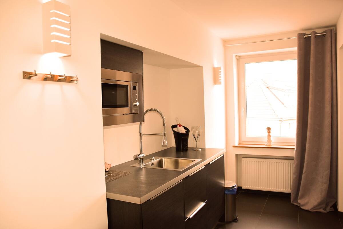 Una cocina moderna con un lavamanos de acero inoxidable, un microondas y un ventanal con vista a un puente.