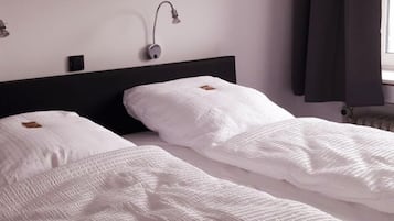 Ein Hotelzimmer mit zwei Betten, einem Bild einer Küstenlandschaft, einem Nachttisch und einem Fenster mit Vorhängen.