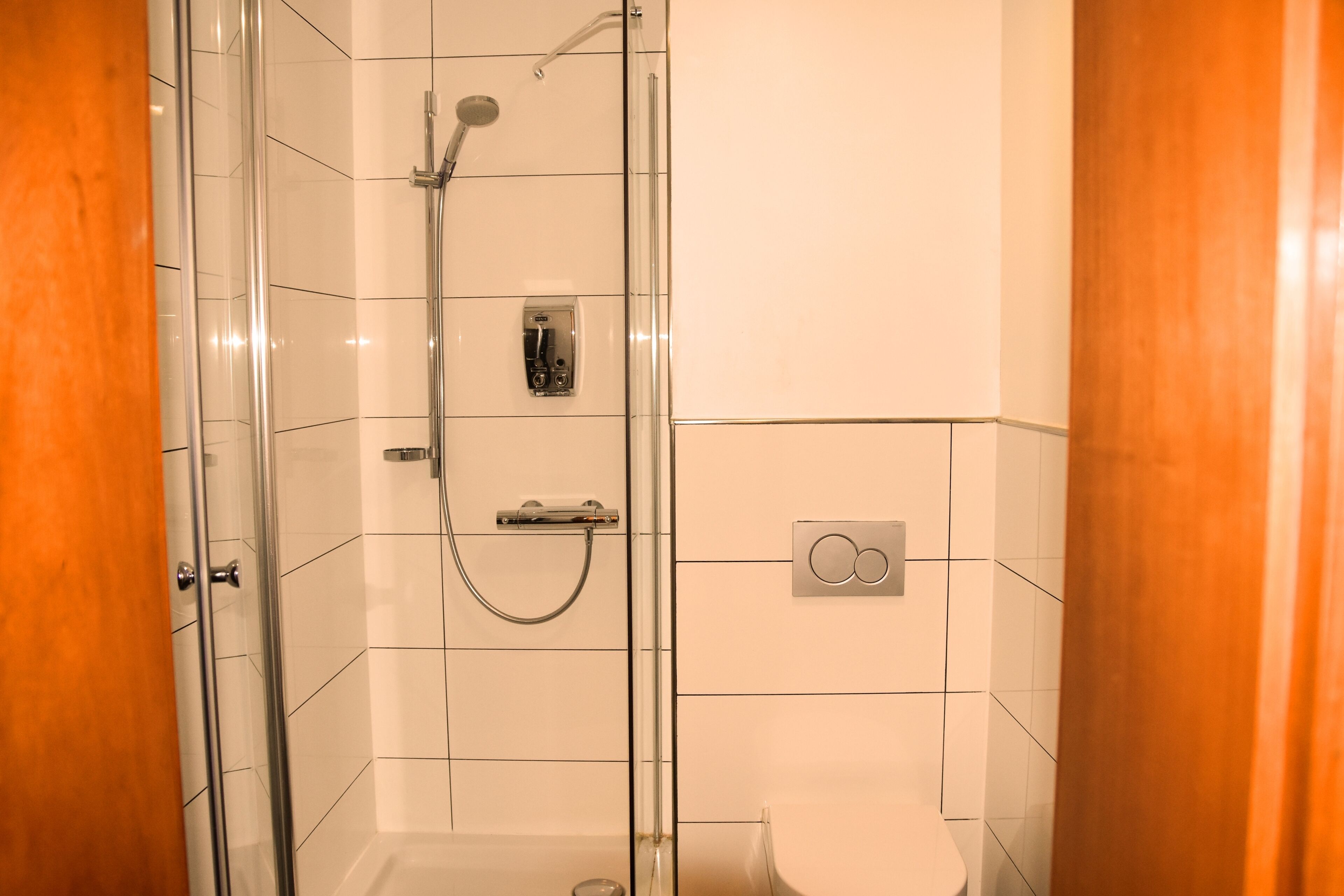 A modern bathroom with a glass-enclosed shower, a toilet, and a control panel.