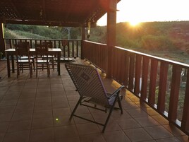 Un espace extérieur abrité, doté d’un sol carrelé, de mobilier en bois et offrant une vue sur un paysage vallonné.