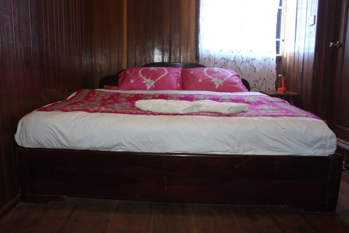 Una cama de madera con una colcha blanca y rosa, una manta blanca y un cabecero de madera.