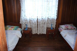 Une chambre à coucher avec deux lits en bois, un plancher en bois et une fenêtre ornée de rideaux en dentelle.