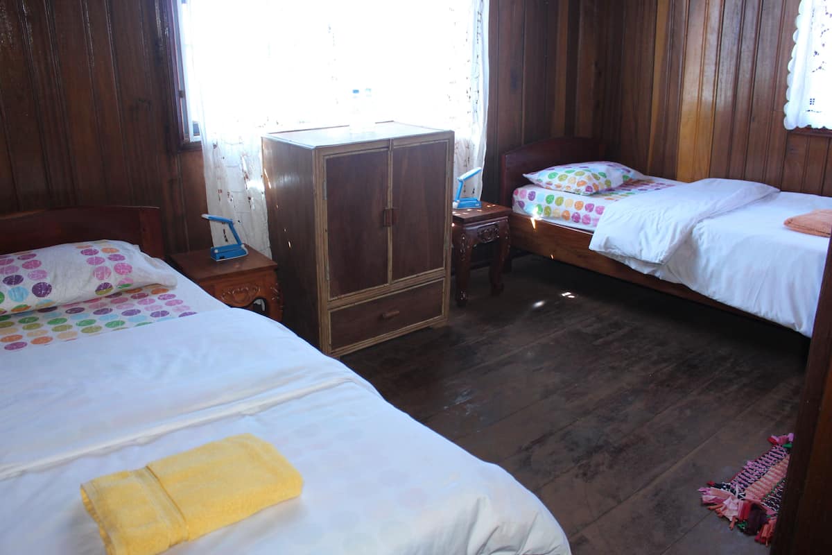 Una habitación con dos camas, paredes de madera, un armario y una pequeña mesa con una lámpara.