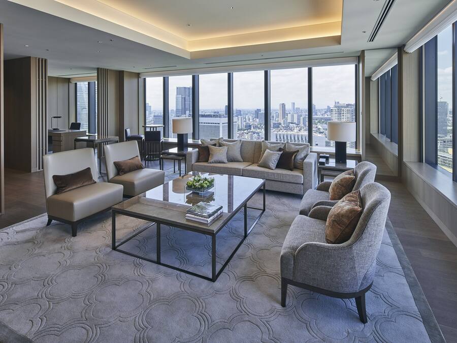 Amplio salón con un sofá grande, sillones y una mesa de centro. Ventanas grandes ofrecen vistas a la ciudad.