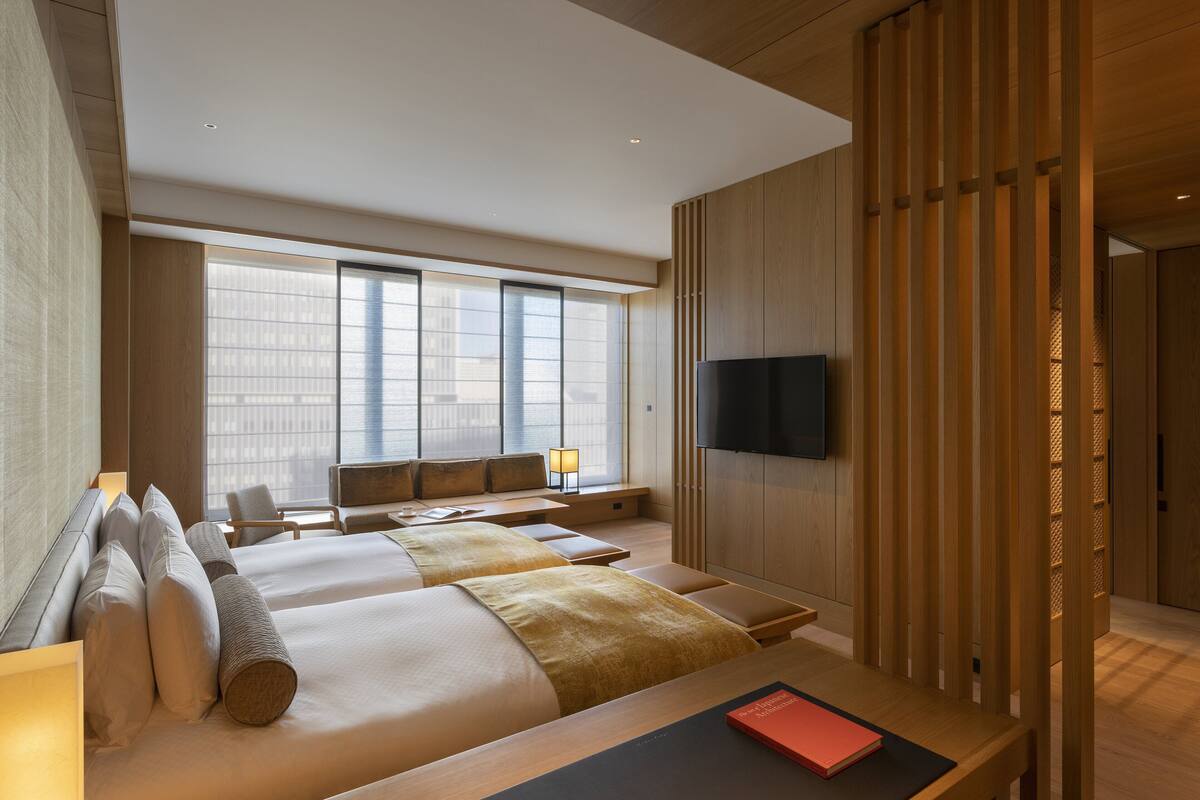 Ett modernt hotellrum med två sängar, en TV, ett skrivbord och ett stort fönster.