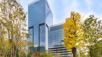 A modern glass building with a reflective facade, surrounded by trees with yellow leaves, indicating an autumn setting.