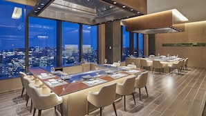 A modern dining area with a large table, multiple chairs, and a city view through large windows. - The Okura Tokyo (Tokyo)
