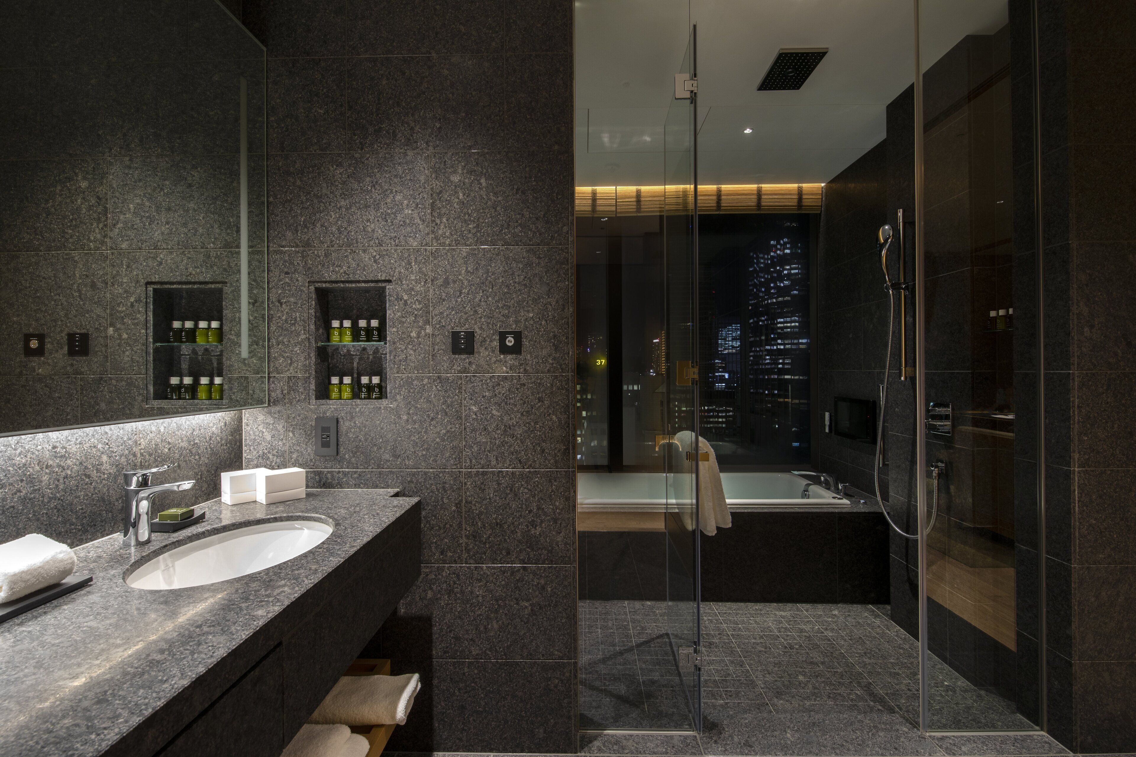 A modern bathroom with a large mirror, granite countertop, and a glass-enclosed shower.