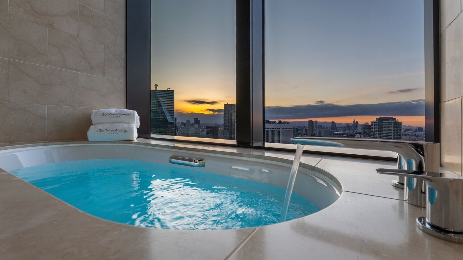 A modern hotel room with a large bathtub, a city view, and a towel rack.