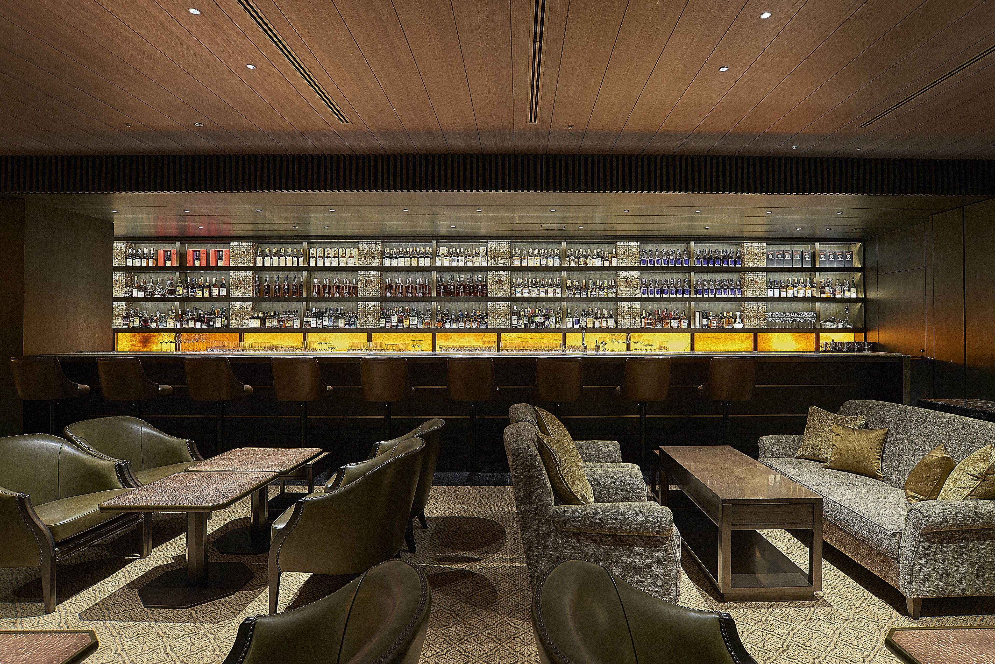 A bar area with multiple seating options, including sofas and chairs, and a well-organized display of bottles.
