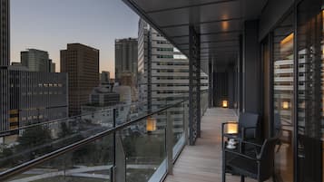 A balcony with a view of city buildings, a glass railing, and a table with chairs.