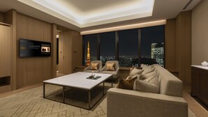 A modern living room with a large window, a flat-screen TV mounted on the wall, and a cityscape view at night. - The Okura Tokyo (Tokyo)