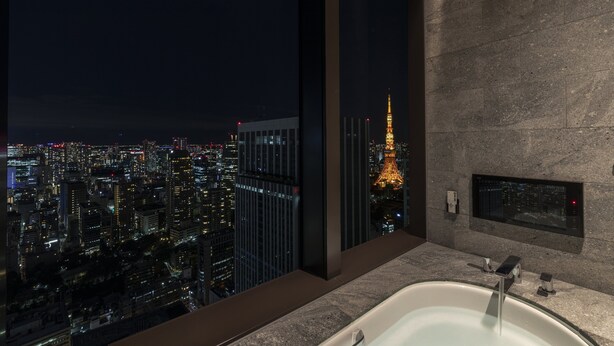 A modern bathroom with a large bathtub, a city view, and a stone wall. - The Okura Tokyo (Tokyo)