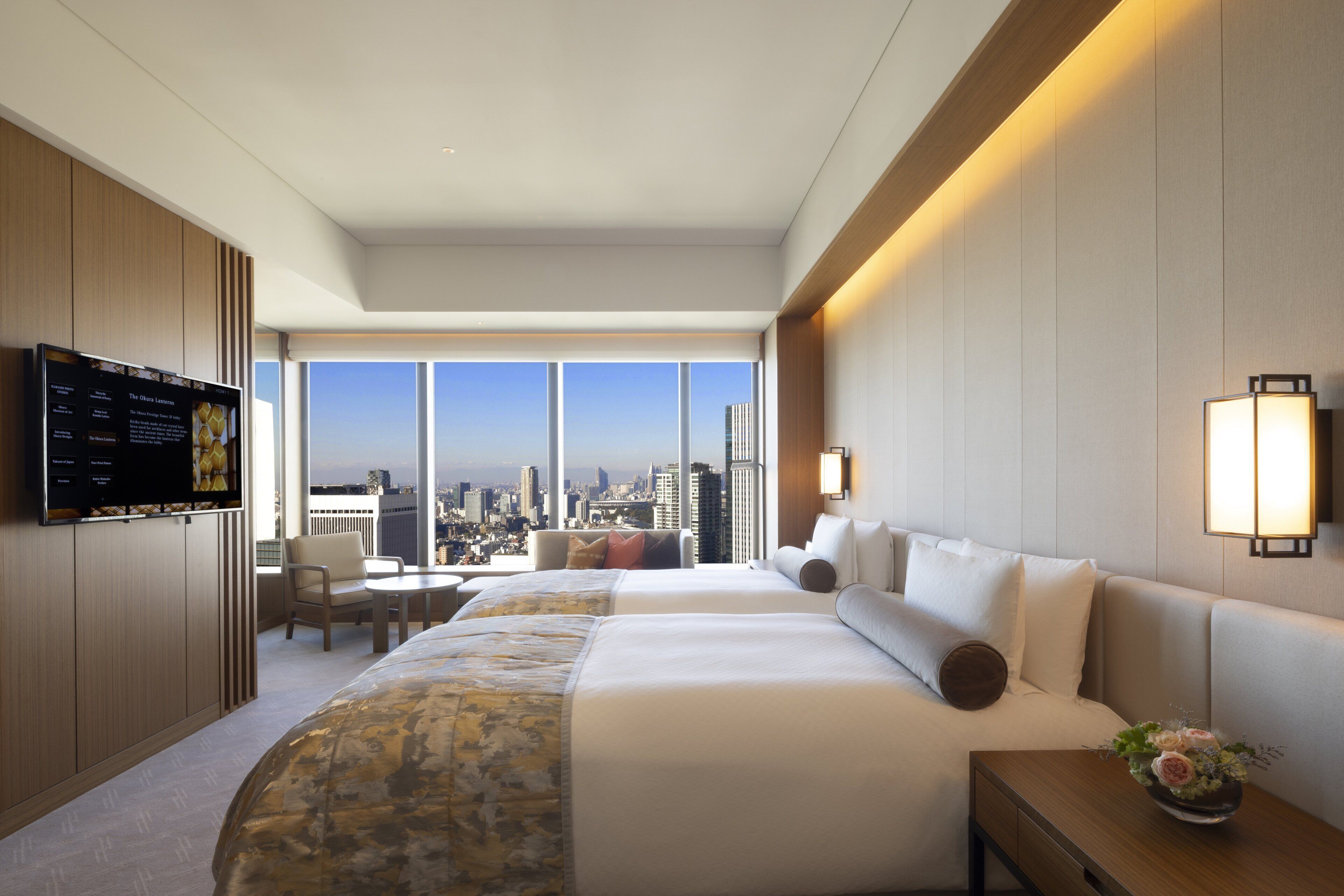 Habitación de hotel con una cama grande, televisión montada en la pared, escritorio con silla y vistas a la ciudad a través de amplios ventanales.