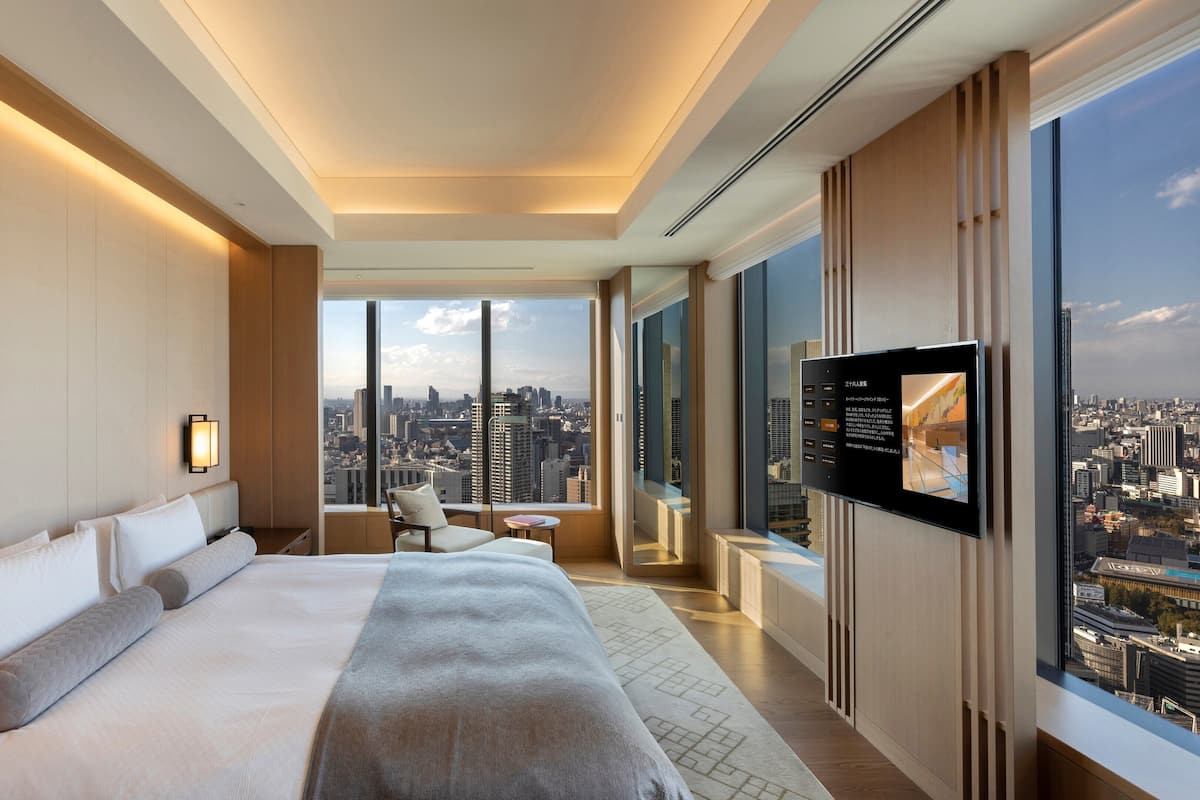 Egy modern szállodai szoba, amelyben egy nagy ágy, egy televízió és kilátás nyílik a városra.