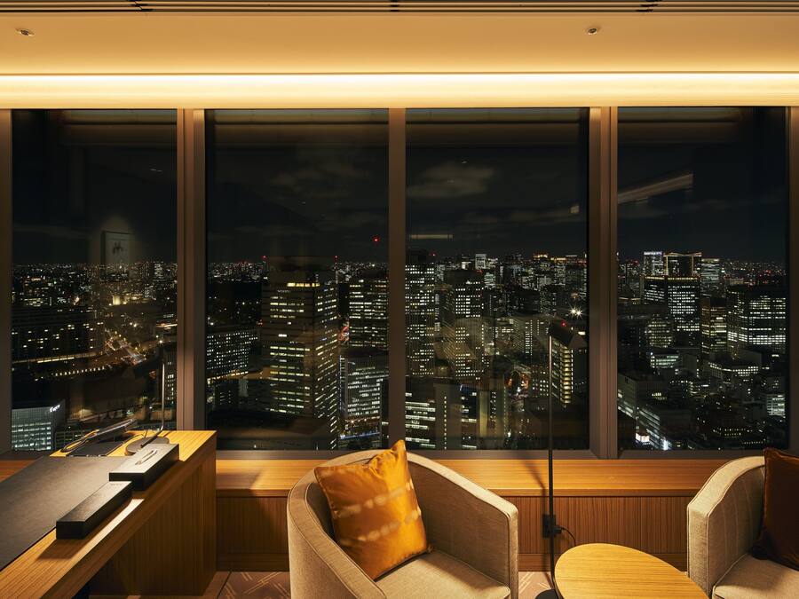 A modern hotel room with a large window offering a cityscape view at night.