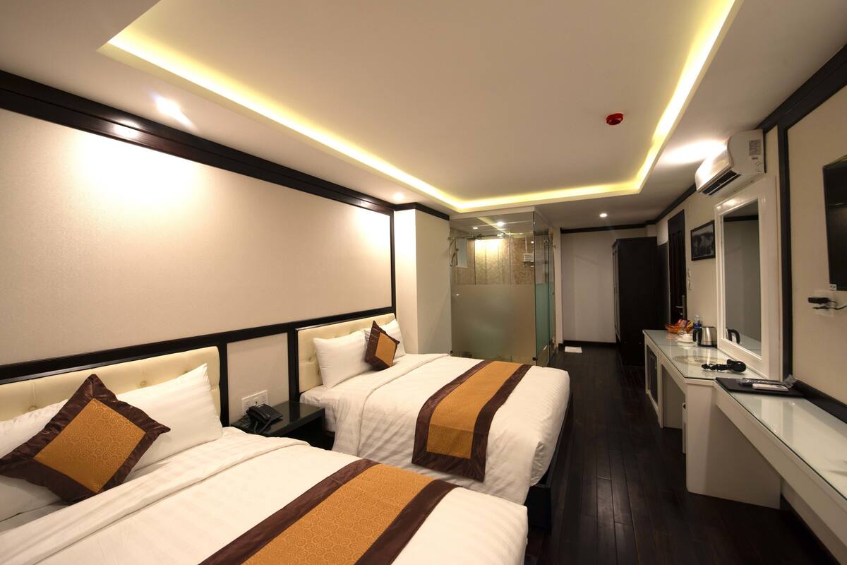 Une chambre d’hôtel avec deux lits, une table de chevet, un miroir et une salle de bain avec douche et toilettes.