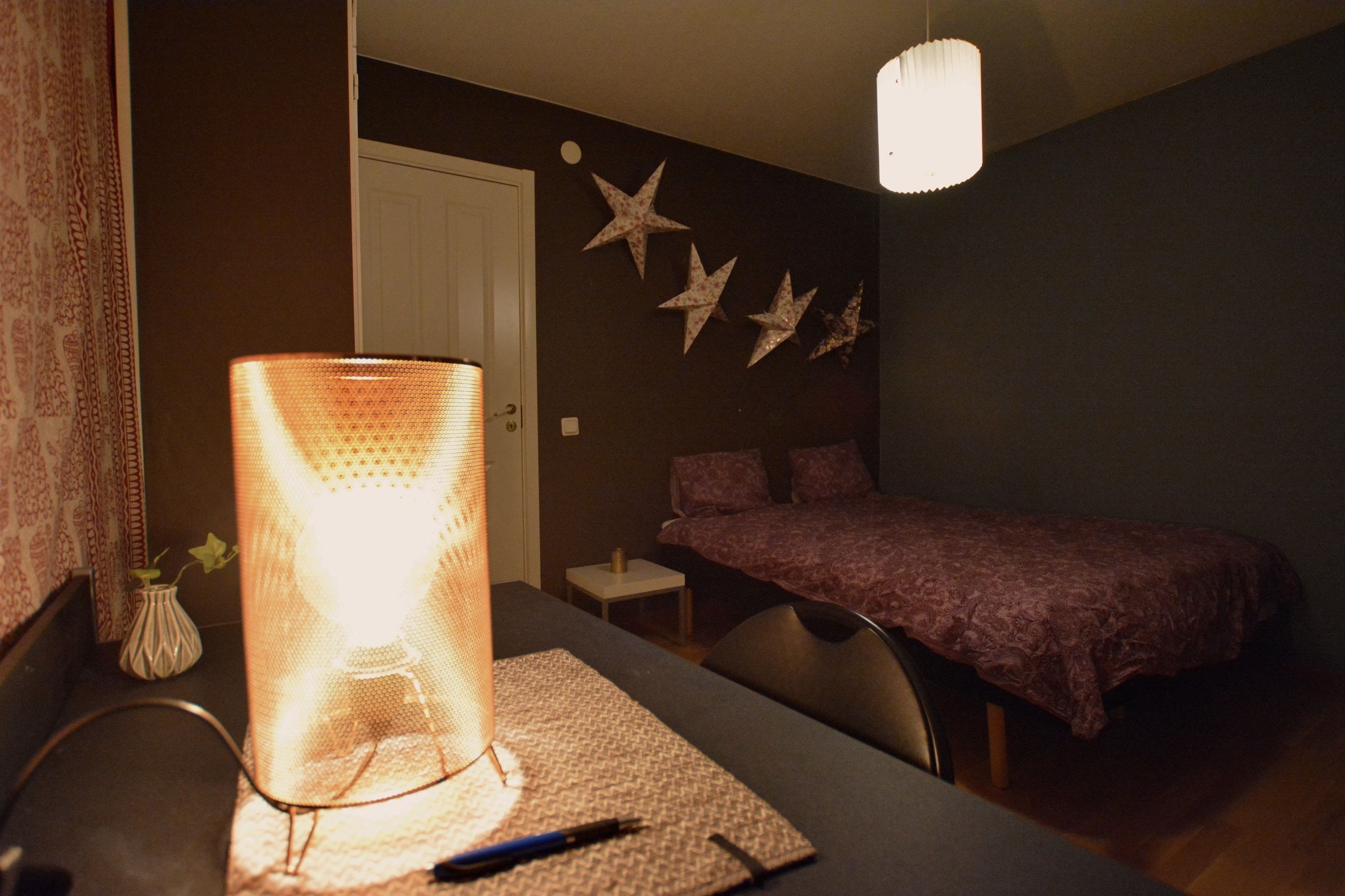A dimly lit room with a bed, a bedside table, and a lamp.
