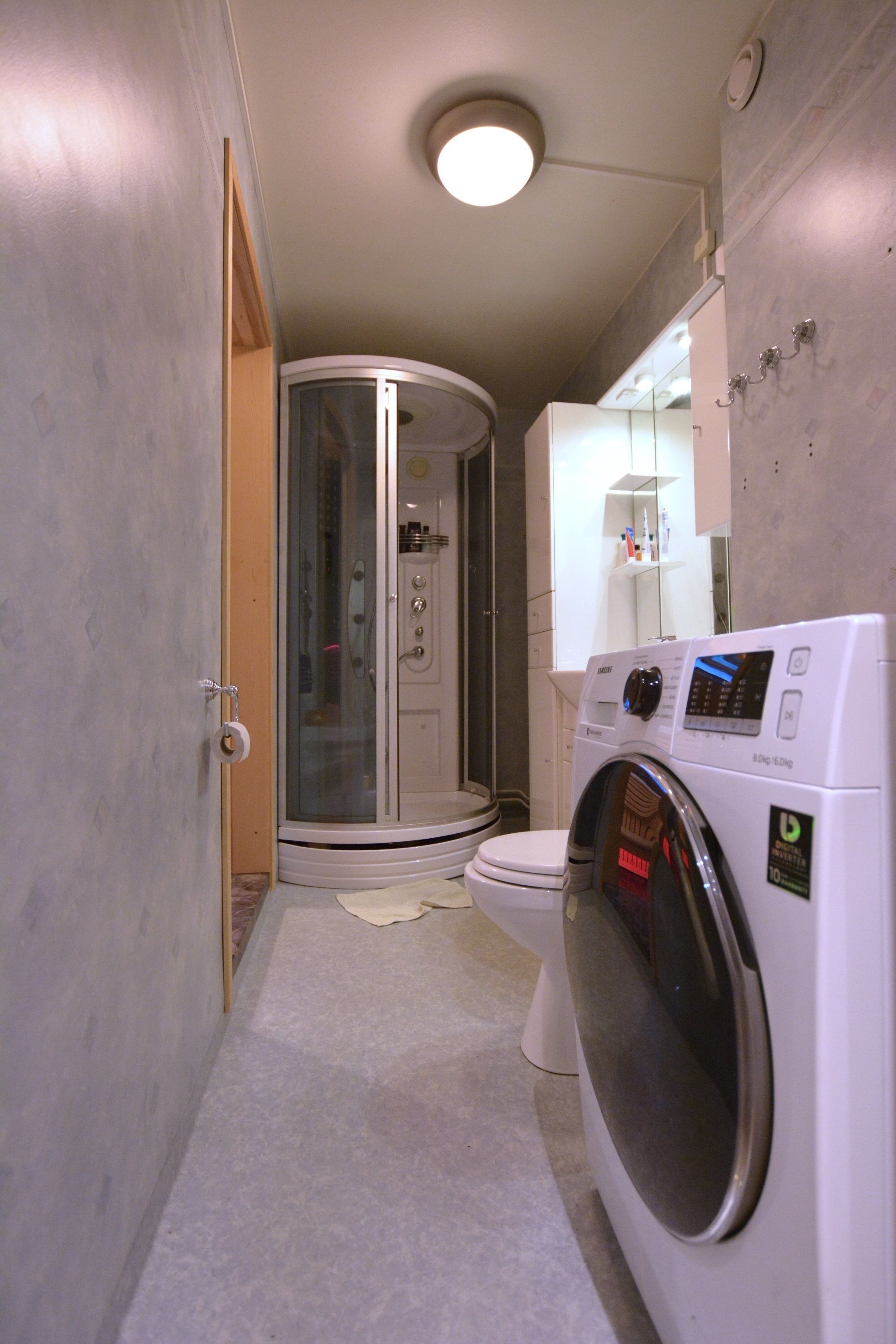 A compact bathroom with a glass shower enclosure, a toilet, and a front-loading washing machine.