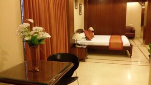 Habitación de hotel con cama, escritorio, silla, mesita de noche, lámpara y un florero con flores.