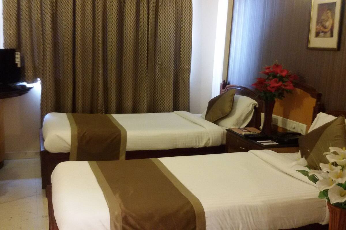 Quarto de hotel com duas camas, uma mesa de escritório com televisão, uma cadeira, uma mesa de cabeceira e um vaso com flores.