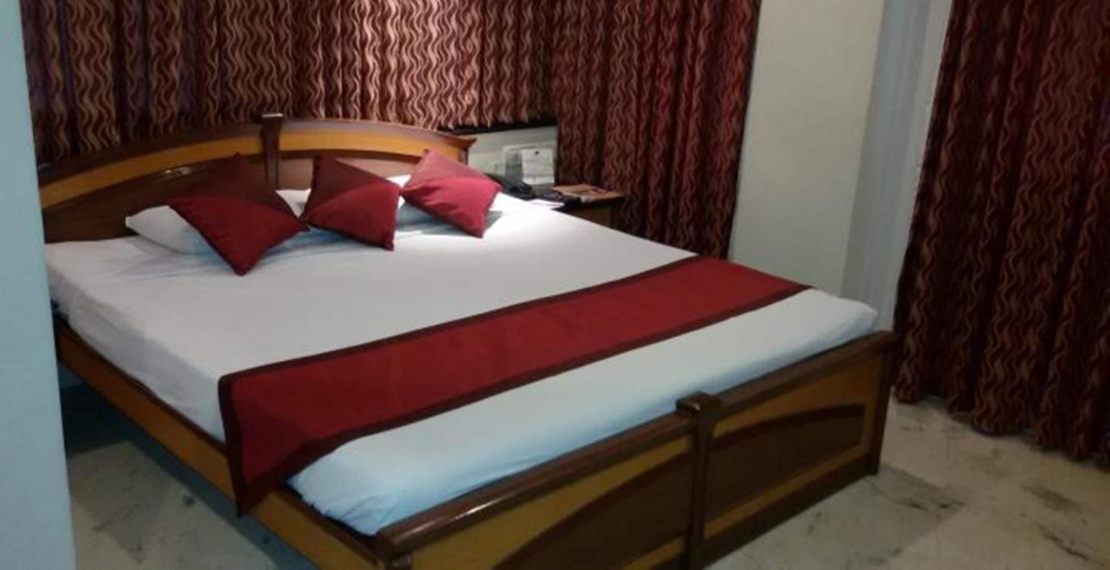 Una cama con estructura de madera, ropa de cama blanca y detalles en rojo.