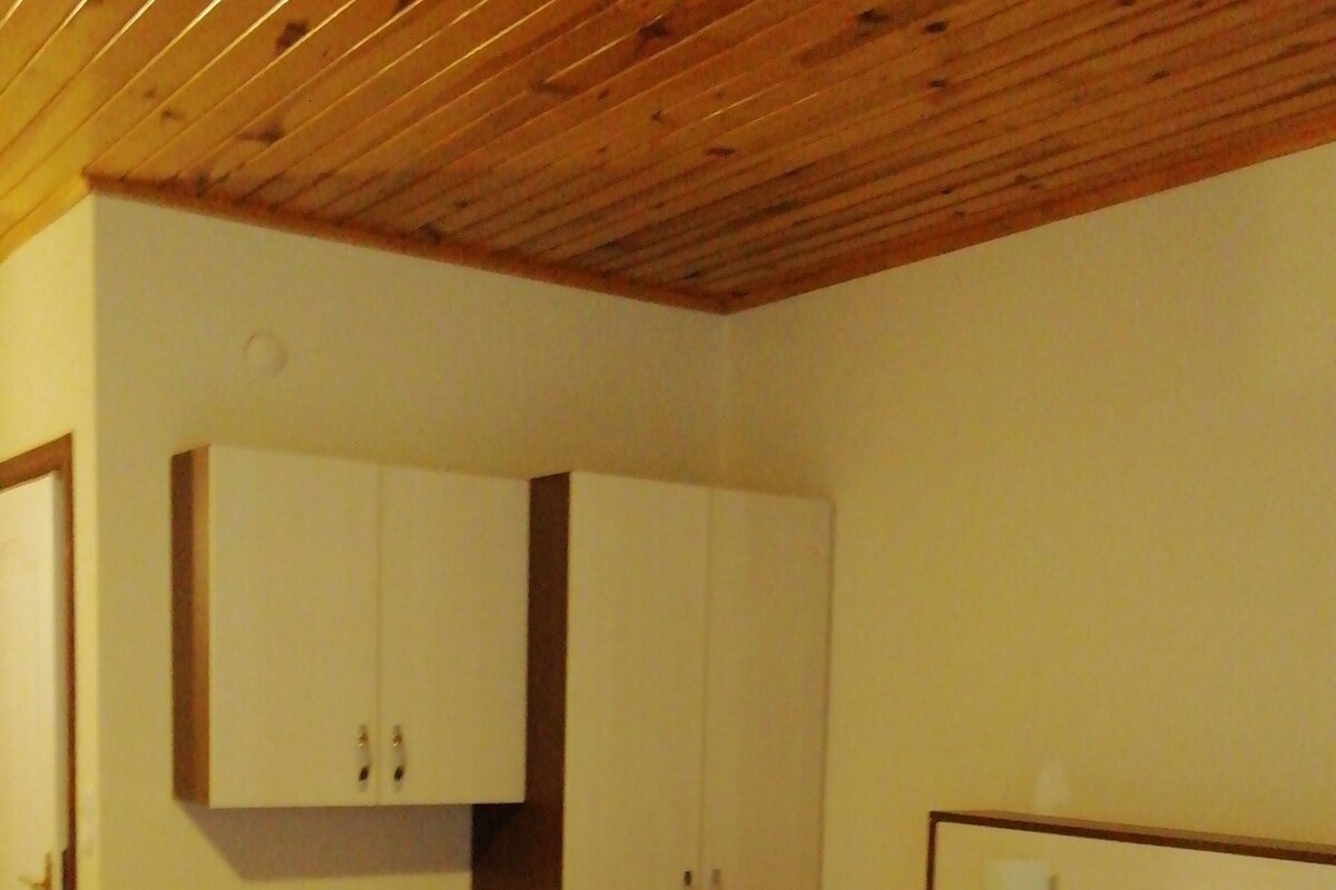 A bedroom with a wooden ceiling, a bed with white bedding, a wardrobe, and a bedside table.