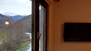 Ein Zimmer mit Fenster, das auf einen Fluss und Berge blickt, einem Wand-Fernseher und einem Holzschrank darunter.