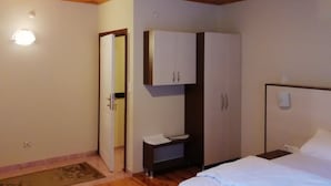 Ein Schlafzimmer mit Holzboden, einem Bett mit weißer Bettwäsche, einem Kleiderschrank und einem kleinen Nachttisch.