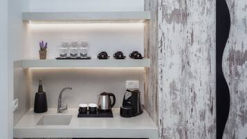 A modern kitchen with a built-in sink, a coffee maker, and a shelf with cups and a plant.