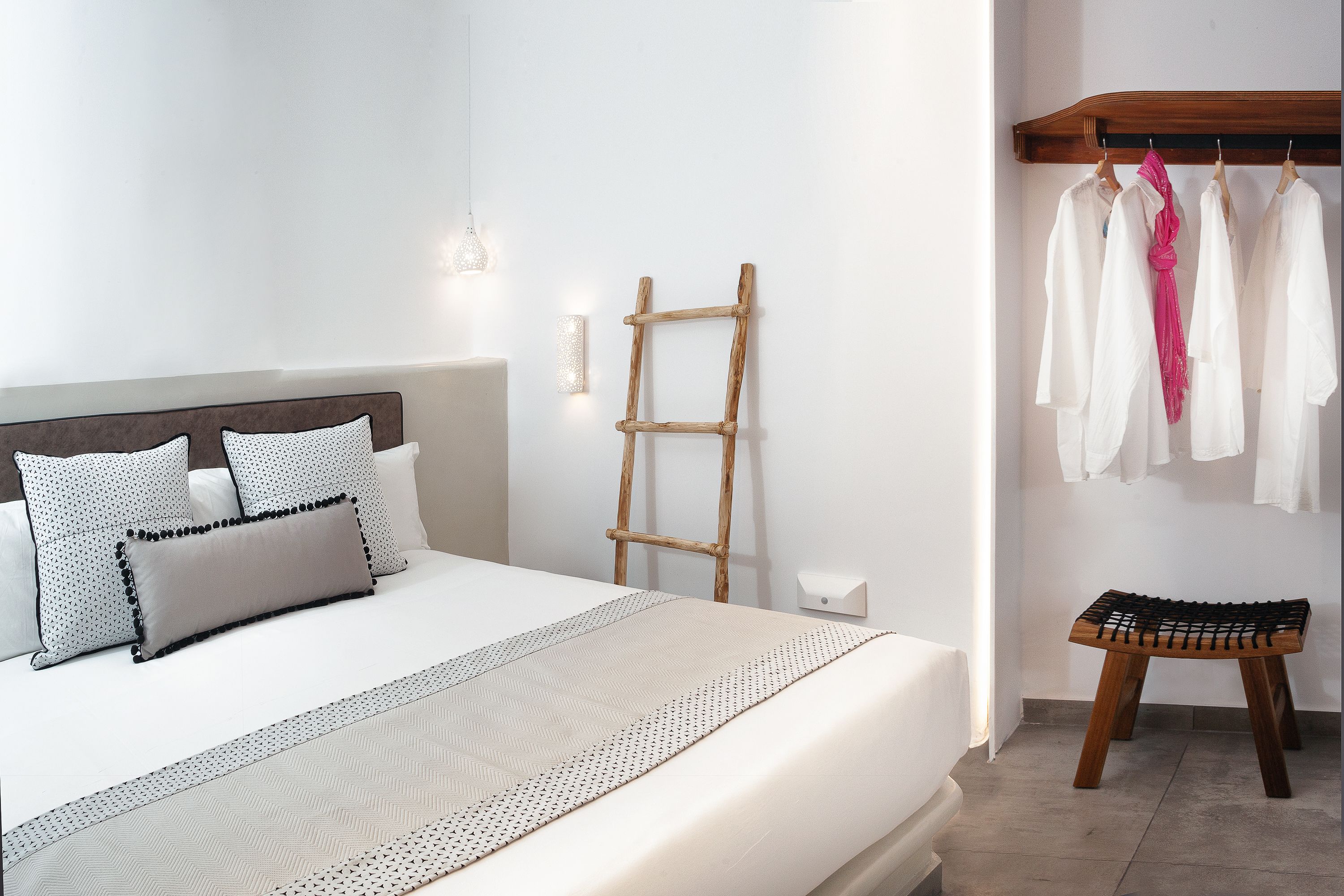 A neatly made bed with a patterned bedspread and pillows, a wooden ladder leaning against the wall, and a small stool with a woven seat.