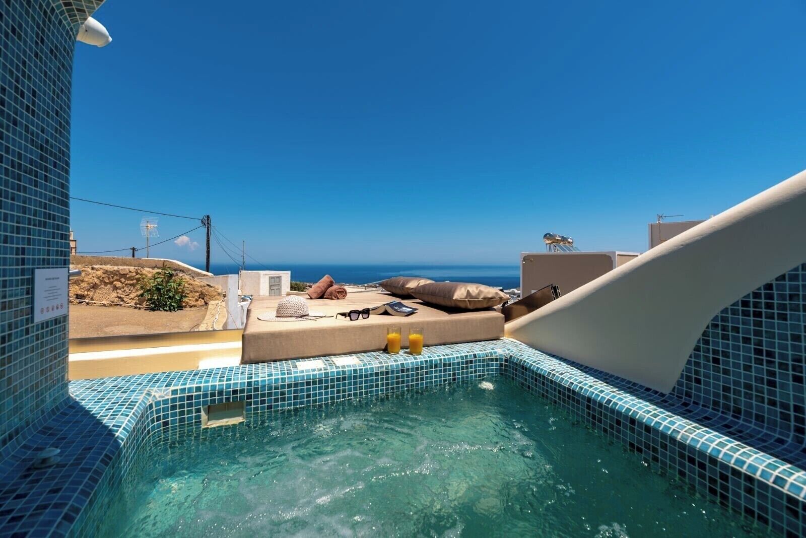 A rooftop pool with a clear view of the ocean, a lounge area with a sofa and pillows, and a tiled pool edge.