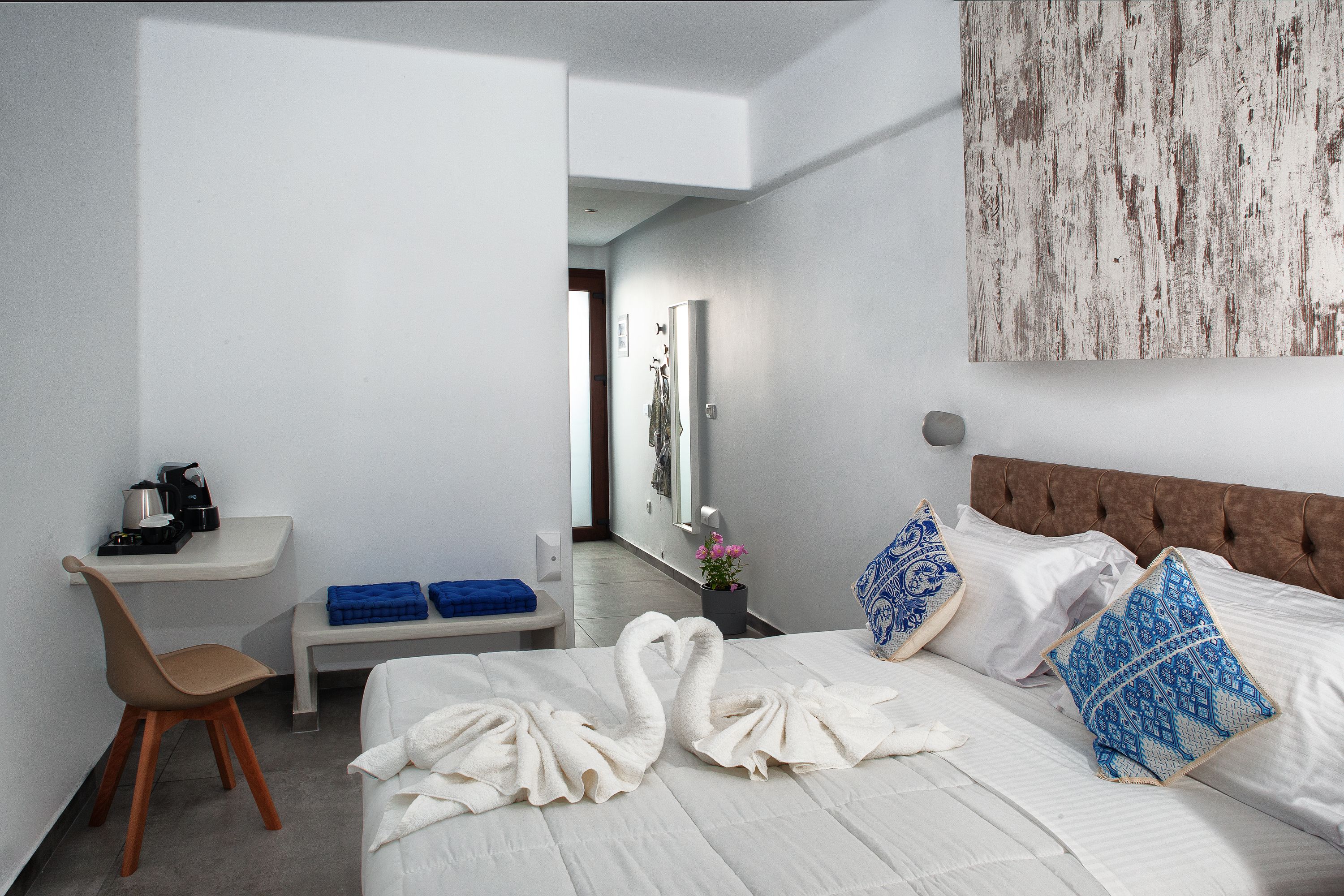 A hotel room with a bed, a desk, a chair, a bench, and a wall-mounted artwork.