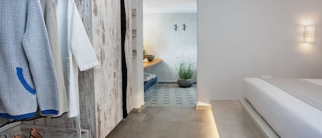 A hallway with a wooden wall, a white sofa, a bed, and a clothing rack with shoes.