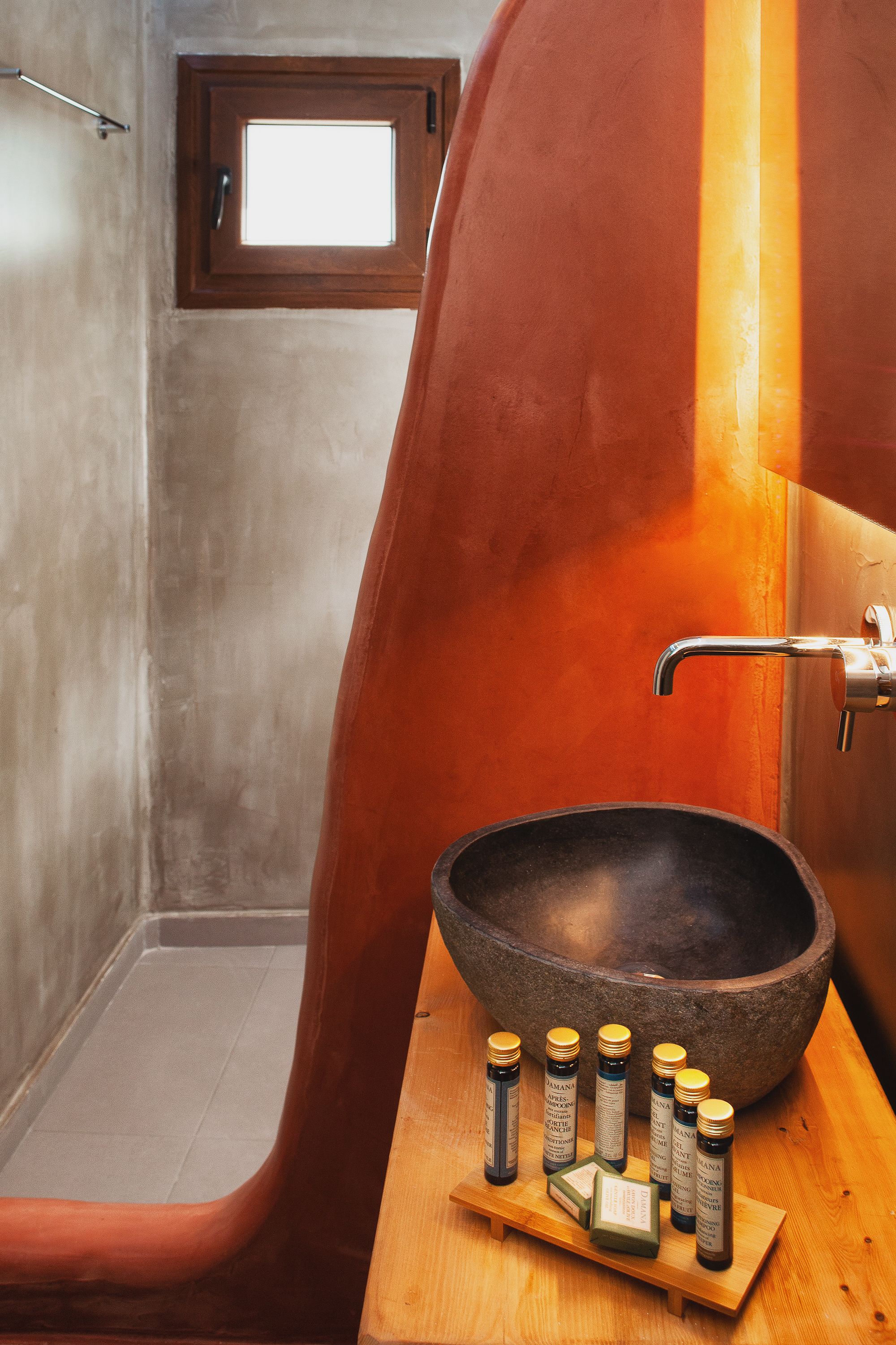 A bathroom with a wooden basin, a large window, and a wooden shelf with bottles.