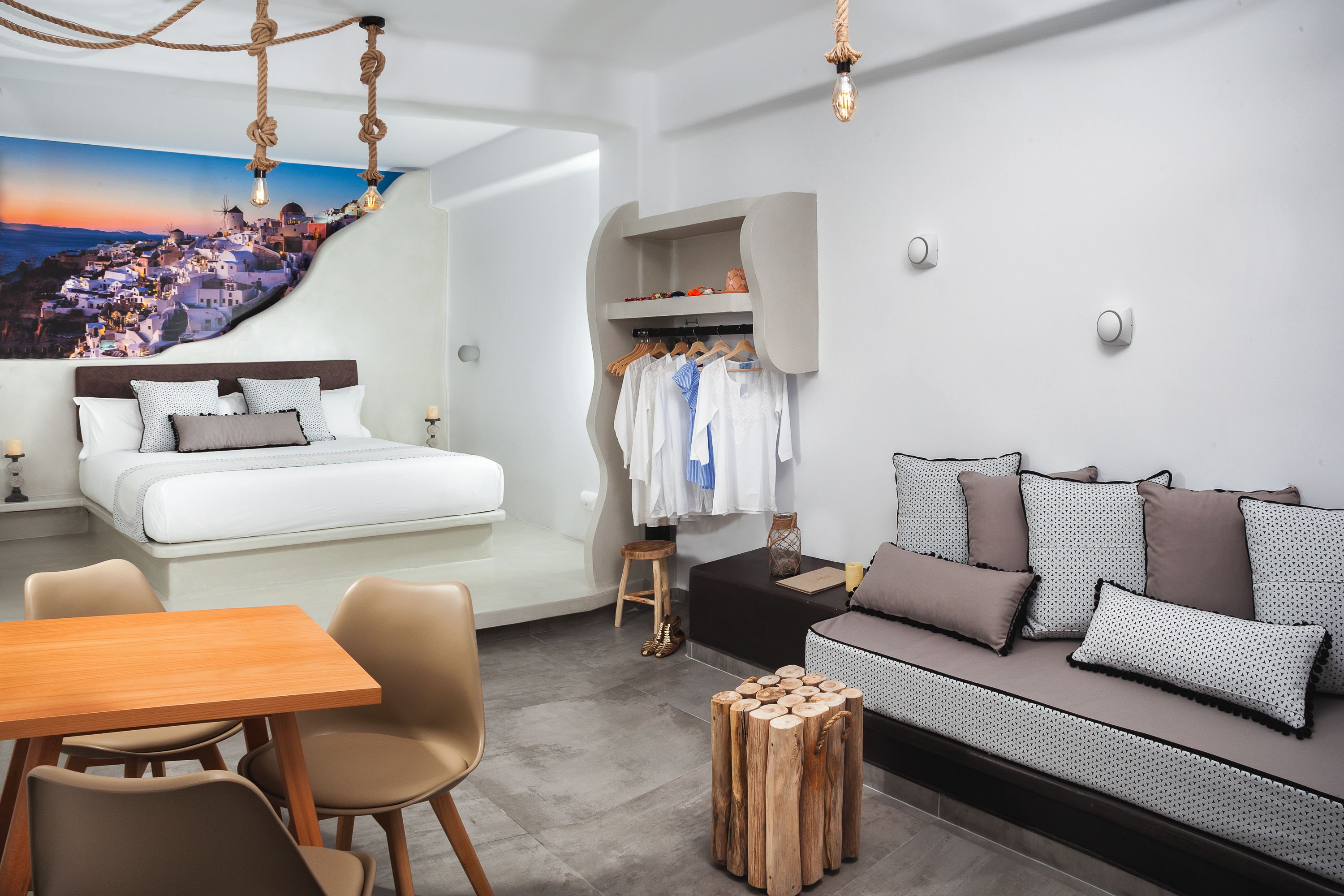 A modern hotel room with a bed, a sofa, a dining area, and a wall with a scenic mural.